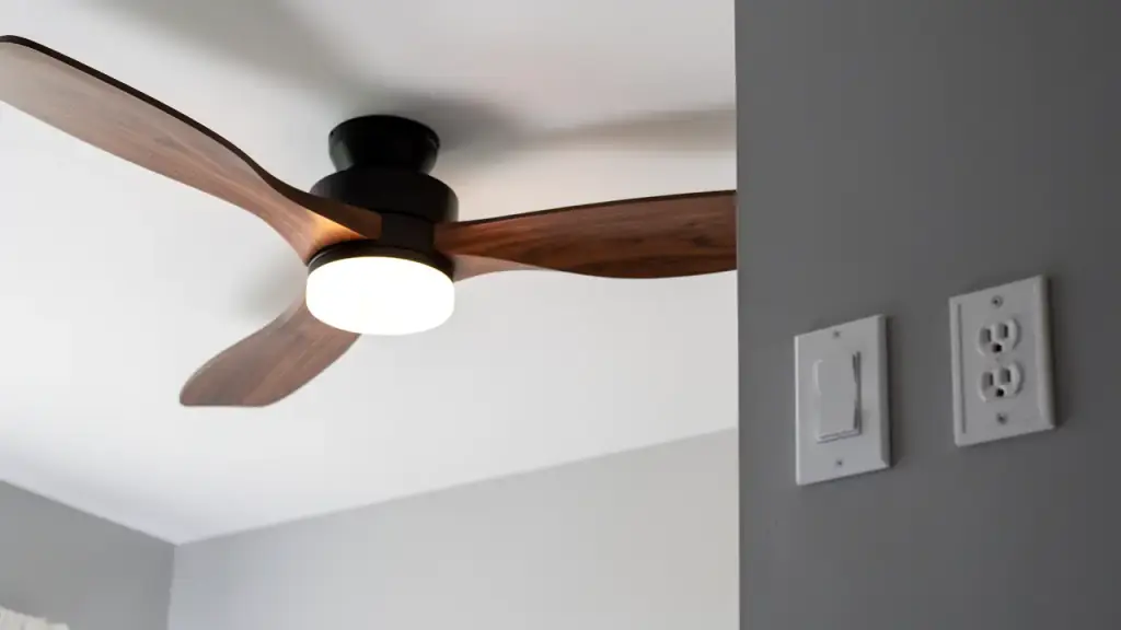 Matte black ceiling fan with walnut blades and a lit light kit beside a switch plate and outlet